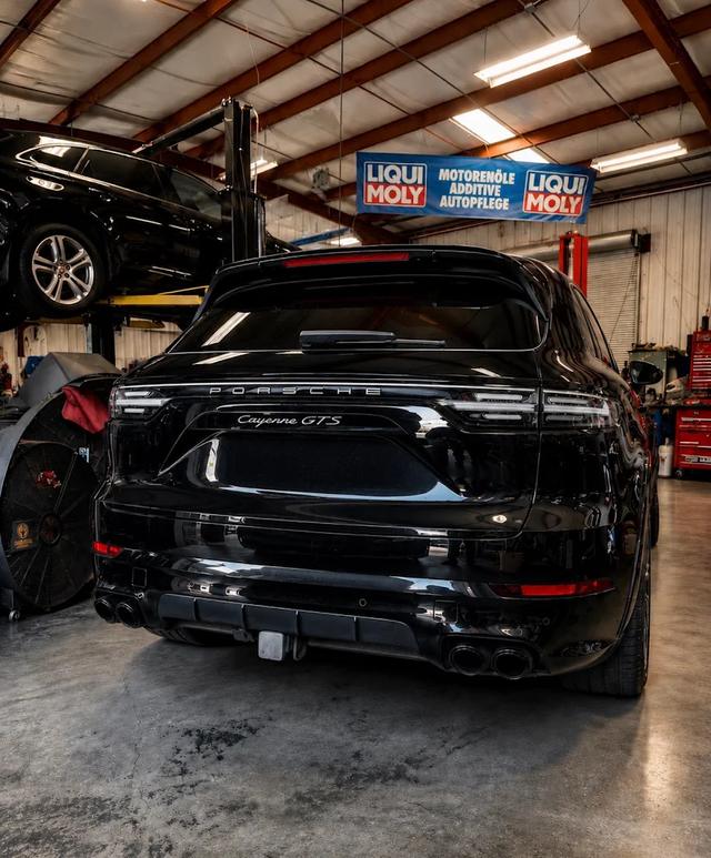Rear of a black Porsche Cayenne GTS in the German Performance shop beside a lift